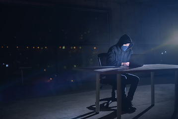 Image showing hacker using laptop computer while working in dark office