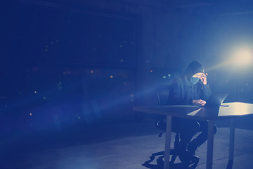 Image showing hacker using laptop computer while working in dark office