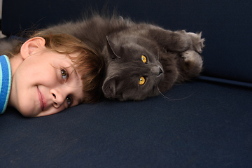 Image showing The girl pressed her head to the cat lying on the sofa