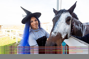 Image showing A girl dressed as a witch shows the face of a horse painted with white paint for the holiday of halloween