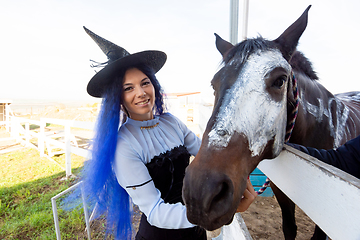 Image showing A girl dressed as a witch shows the face of a horse painted with white paint for the holiday of halloween