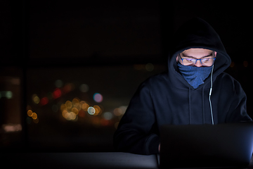 Image showing hacker using laptop computer while working in dark office