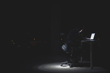 Image showing hacker using laptop computer while working in dark office