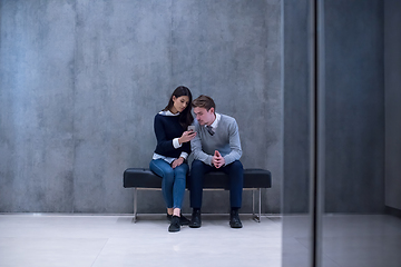 Image showing business couple using mobile phone while sitting on the bench