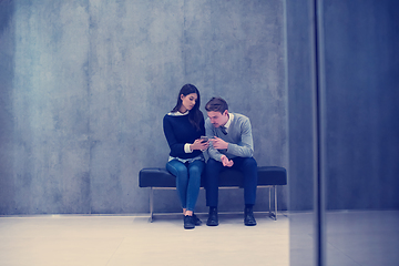 Image showing business couple using mobile phone while sitting on the bench