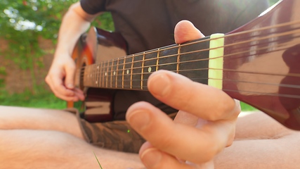 Image showing Man sitting in the grass playing guitar