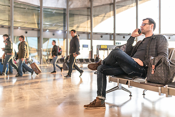 Image showing Casual young male using her cell phone while waiting to board a plane at airport departure gates.