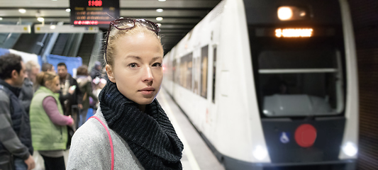 Image showing Young woman in winter coat waiting on the platform of a railway station for train to arrive. Public transport