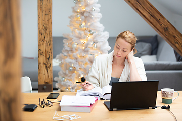 Image showing Young female entrepreneur wearing cosy warm bathrobe working remotly from home in winter Christmas time during 2020 corona virus pandemic. Work from home, selter in place, concept.