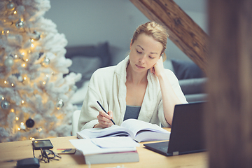 Image showing Young female entrepreneur wearing cosy warm bathrobe working remotly from home in winter Christmas time during 2020 corona virus pandemic. Work from home, selter in place, concept.