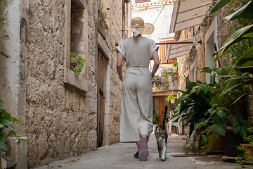 Image showing Rear view of beautiful blonde young female traveler wearing straw sun hat sightseeing and enjoying summer vacation in an old traditional costal town at Adriatic cost, Croatia