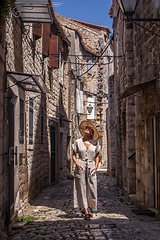 Image showing Beautiful blonde young female traveler wearing straw sun hat sightseeing and enjoying summer vacation in an old traditional costal town at Adriatic cost, Croatia