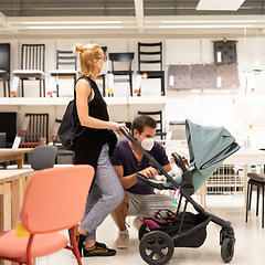 Image showing Young couple with newborn in stroller shopping at retail furniture and home accessories store wearing protective medical face mask to prevent spreading of corona virus when shops reopen