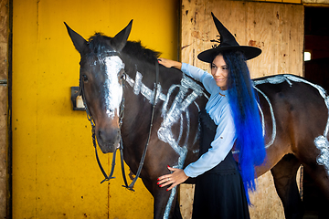 Image showing A girl dressed as a witch stands by a horse on which a skeleton is painted in white paint