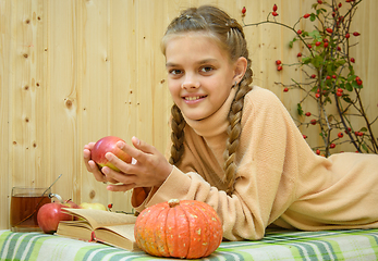 Image showing A girl lying down reads a book, holds an apple in her hands and looks happily into the frame