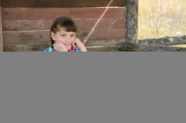 Image showing Portrait of a beautiful girl of ten years old sitting at a wooden table in nature