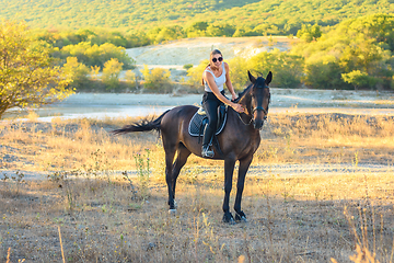 Image showing Girl with glasses strokes a horse riding in the autumn forest