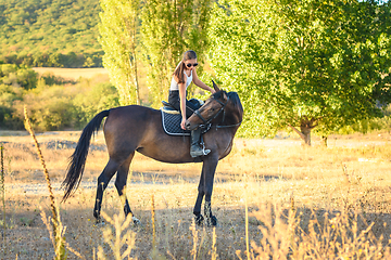 Image showing Girl with glasses feeds a horse with her hand while riding in the autumn forest