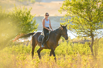 Image showing A girl rides a horse on a warm autumn day