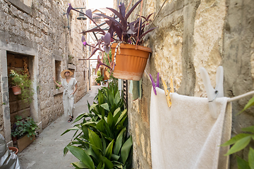 Image showing Beautiful blonde young female traveler wearing straw sun hat sightseeing and enjoying summer vacation in an old traditional costal town at Adriatic cost, Croatia