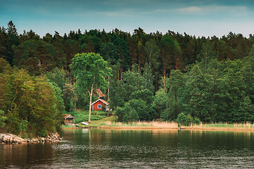 Image showing Sweden. Beautiful Red Swedish Wooden Log Cabin House On Rocky Island Coast In Summer. Lake Or River And Forest Landscape