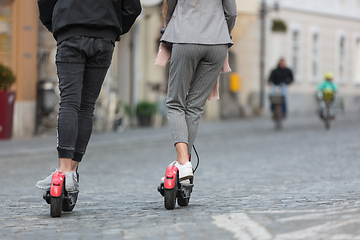 Image showing Rear view of unrecognizable trendy fashinable teenagers riding public rental electric scooters in urban city environment. New eco-friendly modern public city transport in Ljubljana, Slovenia.