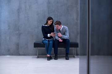 Image showing business couple using mobile phone while sitting on the bench