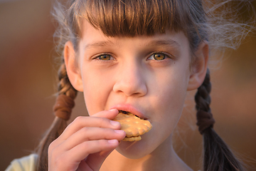 Image showing Cute cheerful little girl is eating cookies at sunset, close-up