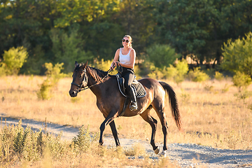Image showing Happy girl walking on a horse in the forest on a warm autumn day