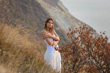 Image showing A girl embraces wildflowers on the background of a beautiful mountain and sea landscape