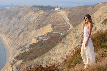 Image showing A girl stands on a mountainside at sunset against a beautiful landscape