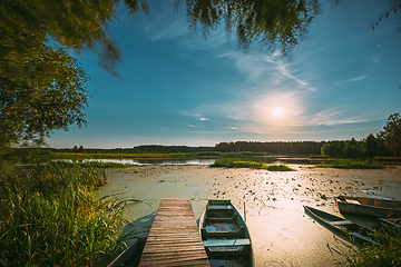 Image showing Real Night Sky Stars And Moonrise Above Old Pier With Moored Wooden Fishing Boat. Natural Starry Sky And Countryside Landscape With Lake River In Early Spring Night. Russian Nature