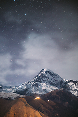 Image showing Stepantsminda, Georgia. Night Starry Sky With Glowing Stars Above Peak Of Mount Kazbek Covered With Snow. Famous Gergeti Church In Night Lightning. Beautiful Georgian Landscape In Late Autumn