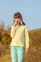 Image showing The girl nibbles on a lollipop and looks at the frame with a puzzled look