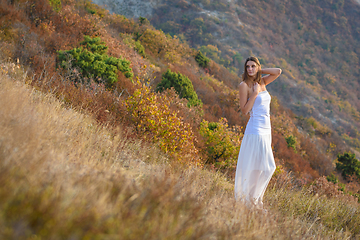 Image showing A beautiful slender girl in white clothes stands on the mountainside