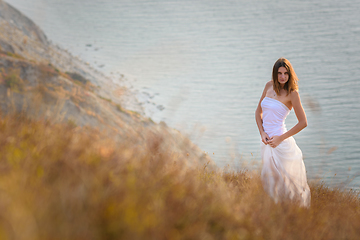 Image showing A beautiful slender girl stands on a hillock against the background of the sea