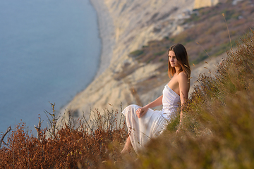 Image showing A beautiful girl in a white dress enjoys a beautiful view from the mountain to the sea at sunset