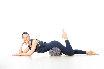 Image showing Restorative yoga with a bolster. Young sporty female yoga instructor in bright white yoga studio, lying on bolster cushion, stretching, smilling, showing love and passion for restorative yoga