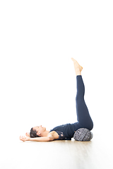 Image showing Restorative yoga with a bolster. Young sporty attractive woman in bright white yoga studio, lying on bolster cushion, stretching and relaxing during restorative yoga. Healthy active lifestyle