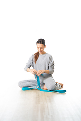 Image showing Young sporty female yoga instructor in bright white yoga studio, smiling cheerfully while preparing yoga exercise props