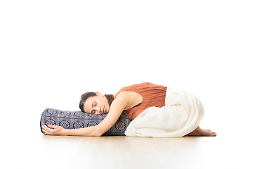 Image showing Restorative yoga with a bolster. Young sporty attractive woman in bright white yoga studio, lying on bolster cushion, stretching and relaxing during restorative yoga. Healthy active lifestyle