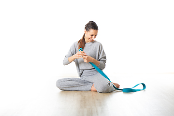 Image showing Young sporty female yoga instructor in bright white yoga studio, smiling cheerfully while preparing yoga exercise props