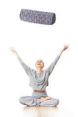 Image showing Restorative yoga with a bolster. Young sporty female yoga instructor in bright white yoga studio, throwing bolster cushion in air , smilling, showing love and passion for restorative yoga