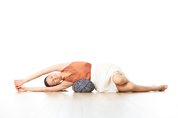 Image showing Restorative yoga with a bolster. Young sporty attractive woman in bright white yoga studio, lying on bolster cushion, stretching and relaxing during restorative yoga. Healthy active lifestyle