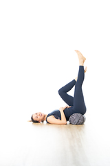 Image showing Restorative yoga with a bolster. Young sporty attractive woman in bright white yoga studio, lying on bolster cushion, stretching and relaxing during restorative yoga. Healthy active lifestyle