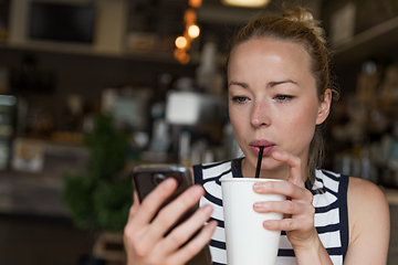 Image showing Thoughtful woman reading news on mobile phone while sipping coffee in coffee shop.