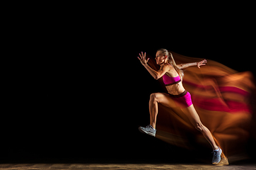 Image showing Professional female relay racer training on black studio background in mixed light