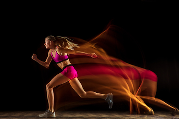 Image showing Professional female relay racer training on black studio background in mixed light