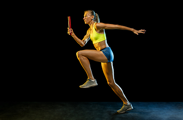 Image showing Professional female relay racer training on black studio background in neon light