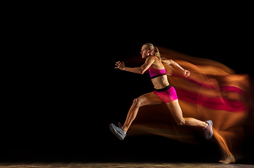 Image showing Professional female relay racer training on black studio background in mixed light